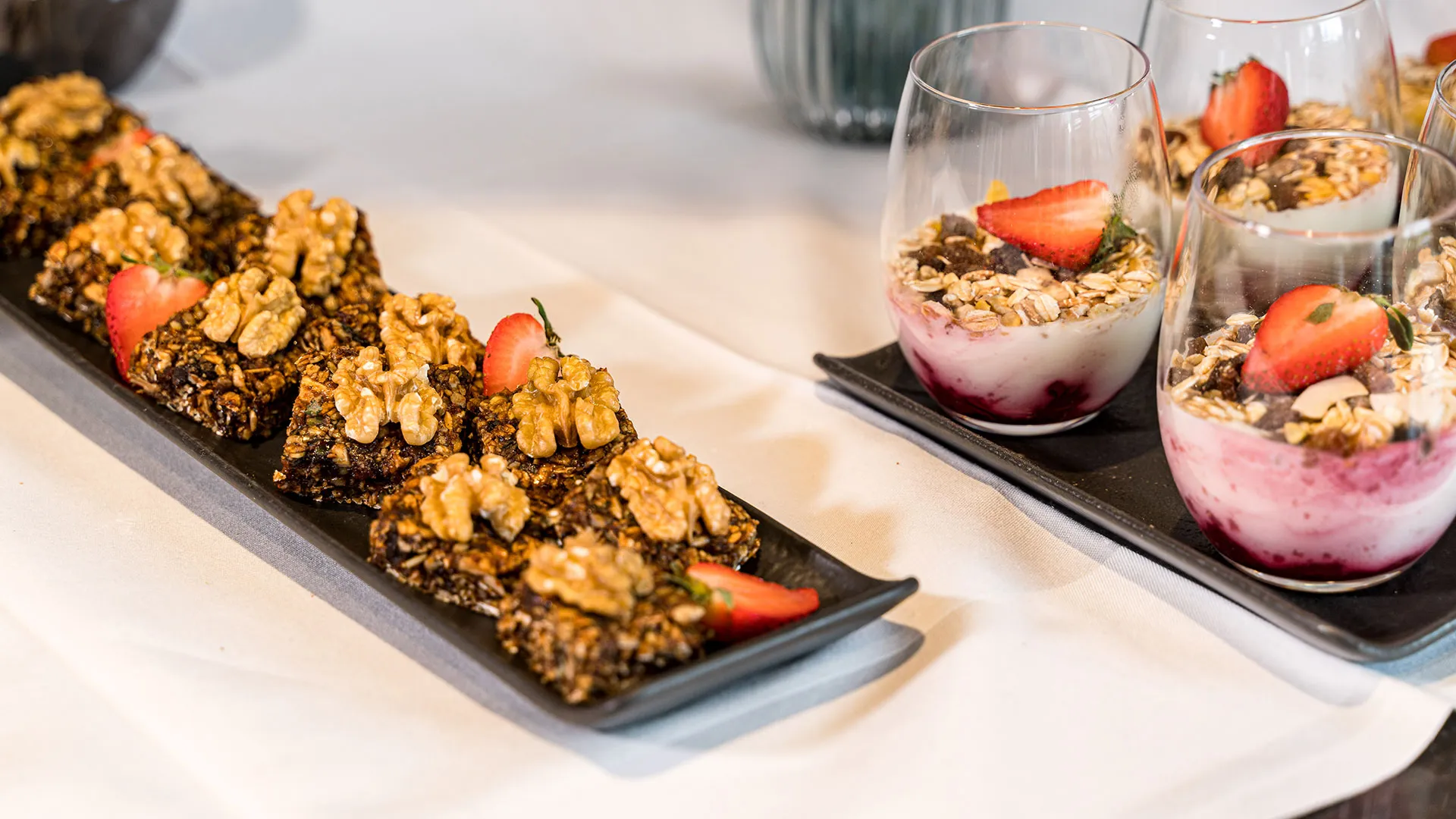 Müsliriegel mit Walnüssen und Erdbeeren neben Joghurt-Dessertgläsern mit Beeren und Granola
