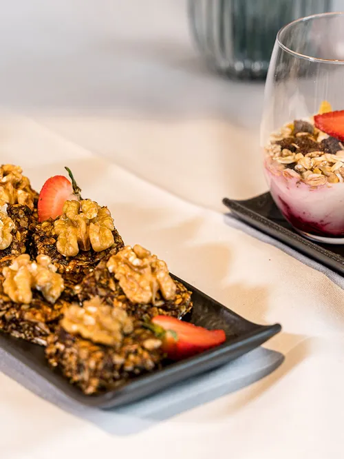 Müsliriegel mit Walnüssen und Erdbeeren neben Joghurt-Dessertgläsern mit Beeren und Granola