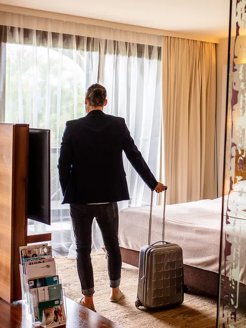 Mann mit Koffer im Hotelzimmer blickt aus dem Fenster