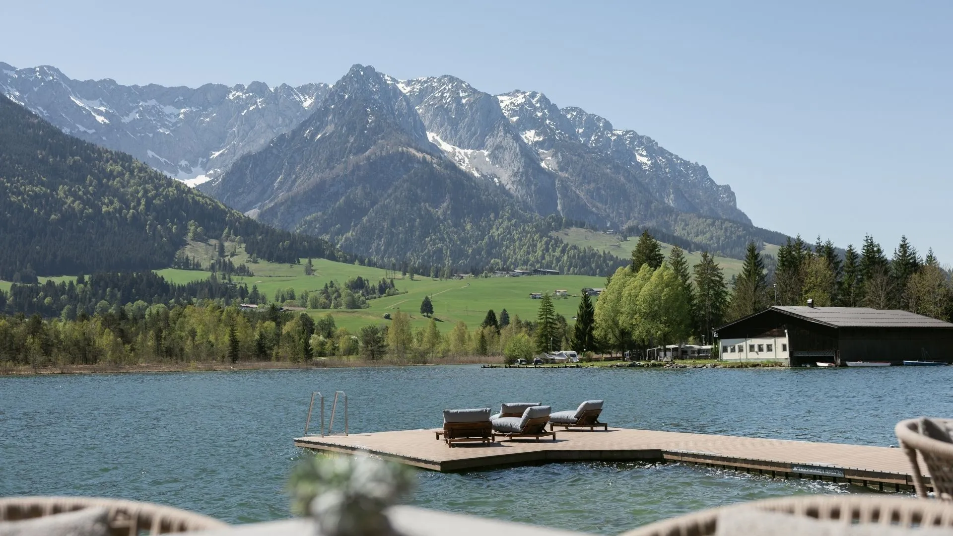Liegestühle auf Steg am See mit Bergpanorama im Hintergrund