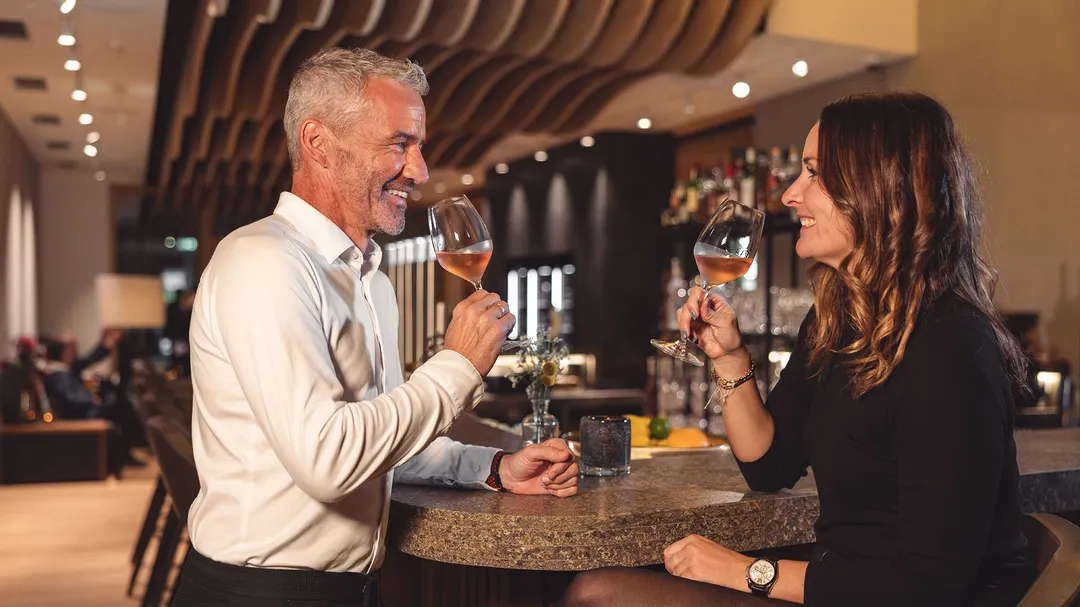 Paar stößt mit Weingläsern an der Hotelbar an