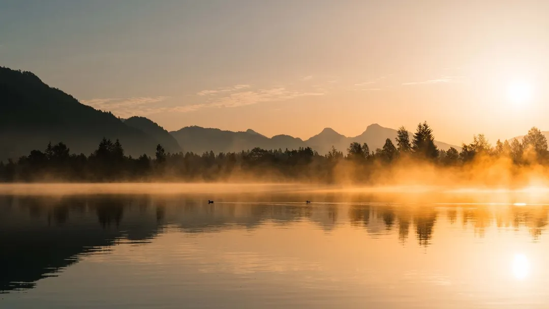 Nebel über einem See bei Sonnenaufgang vor Bergkulisse