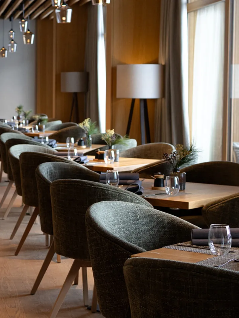 Modernes Restaurant mit Holzböden, gedeckten Tischen, dunkelgrünen Stühlen, einer Lamellenholzdecke und stilvollen Pendelleuchten.