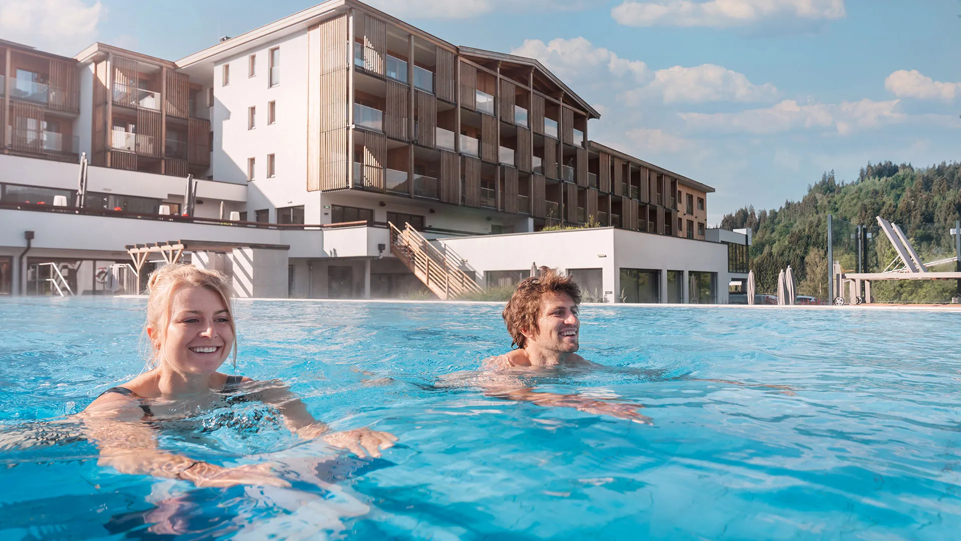 Paar schwimmt im Außenpool vor dem Hotel Das Hohe Salve