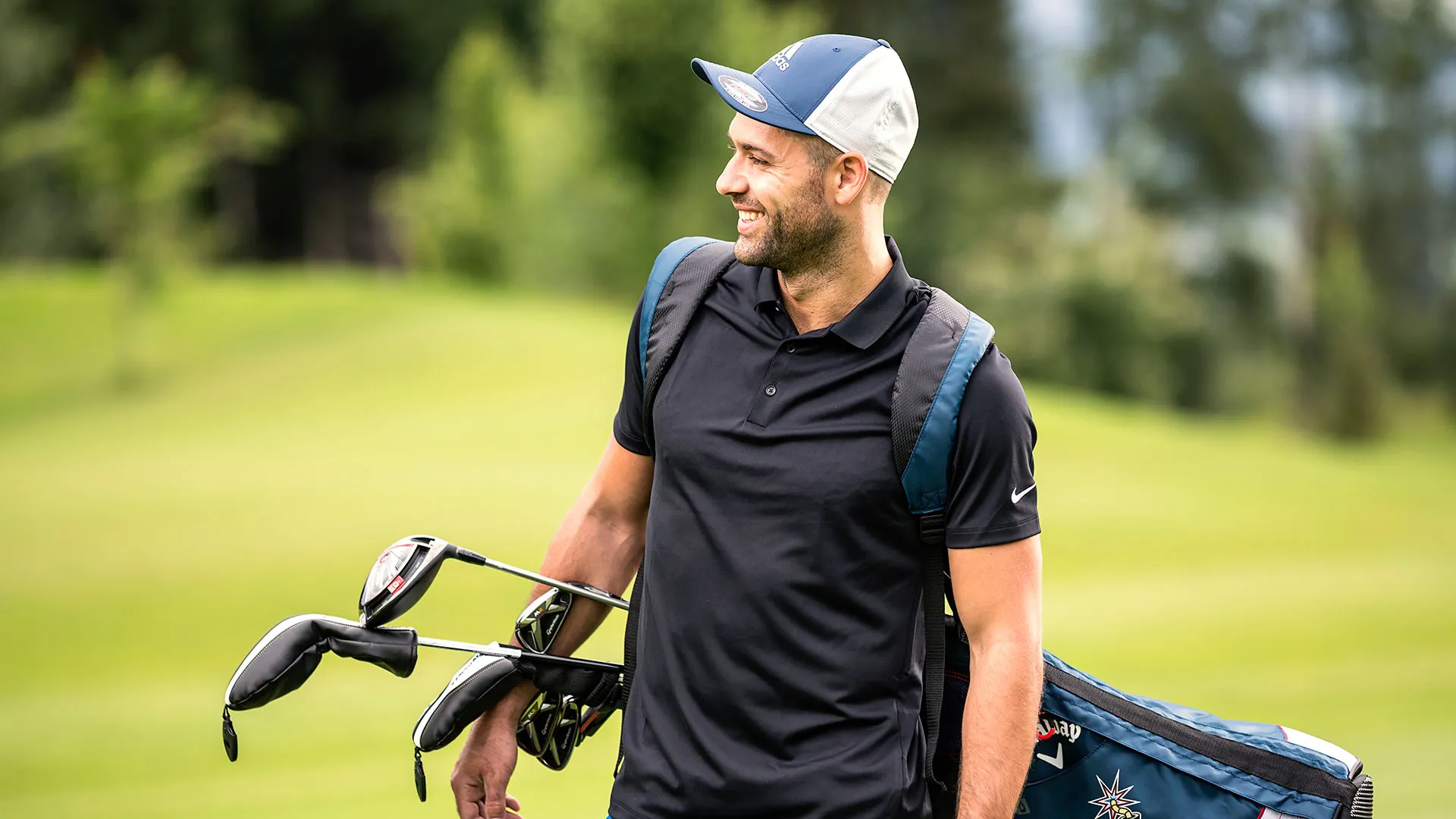 Lächelnder Mann mit Golftasche und Kappe auf dem Golfplatz