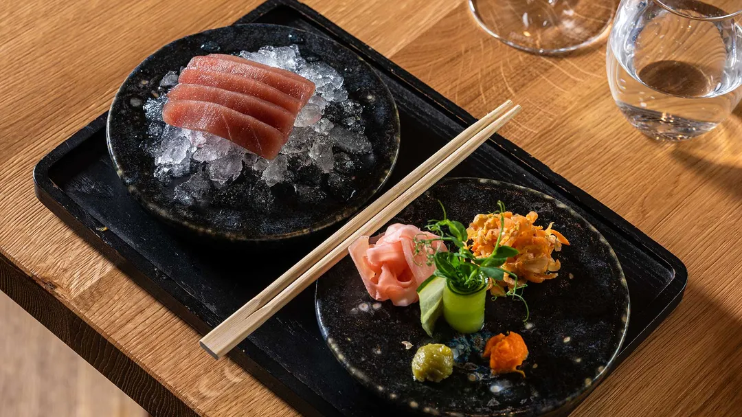 Thunfisch-Sashimi auf Eis und Beilagen wie Ingwer und Wasabi auf schwarzen Tellern