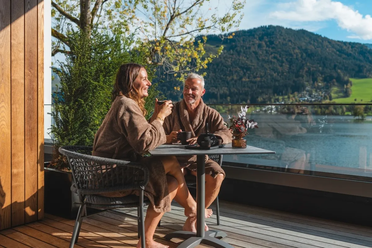 Paar in Bademänteln beim Kaffee auf Balkon mit Seeblick