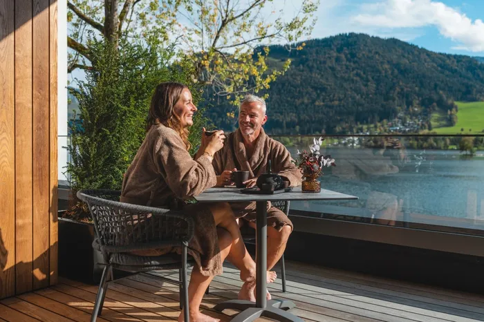 Paar in Bademänteln beim Kaffee auf Balkon mit Seeblick