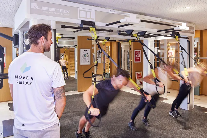 Gruppentraining mit Schlingentrainer im Fitnessraum, Trainer beobachtet