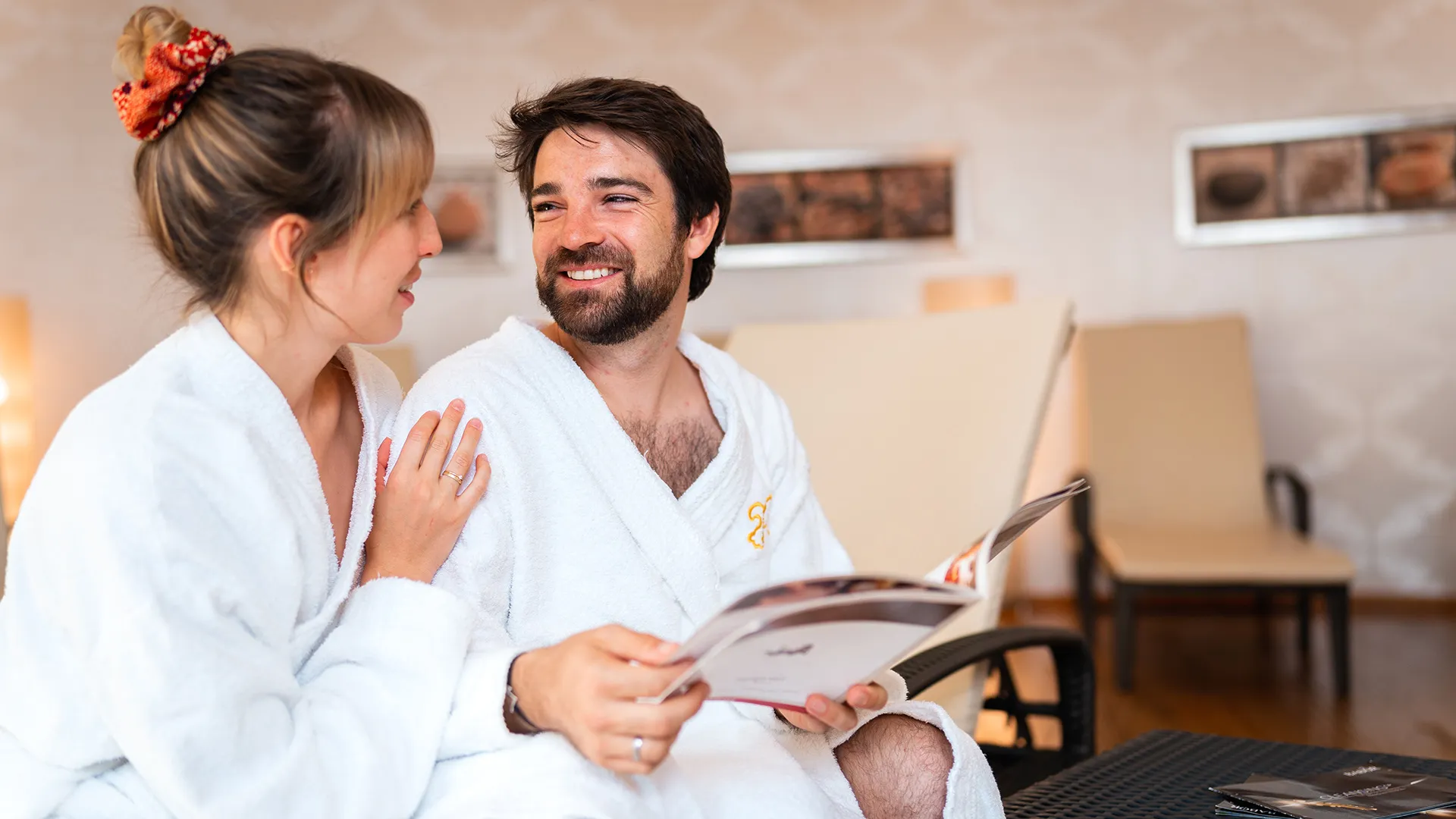 Paar in Bademänteln entspannt im Wellnessbereich mit Zeitschrift