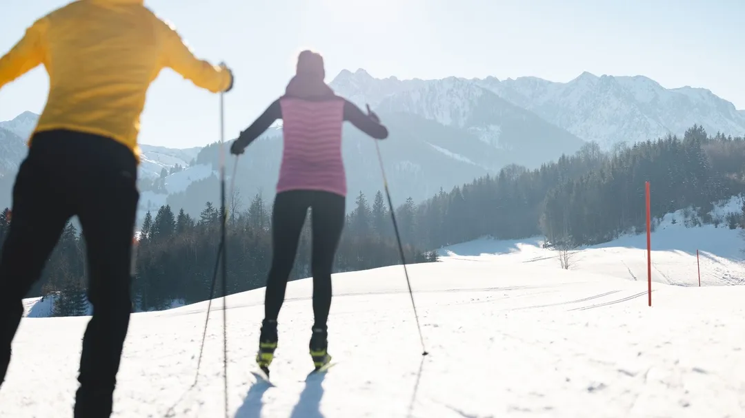 Zwei Langläufer auf verschneiter Loipe vor Bergpanorama