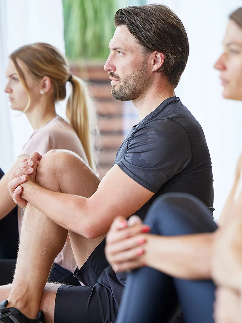 Gruppe sitzt im Schneidersitz während einer Yogastunde im Fitnessraum