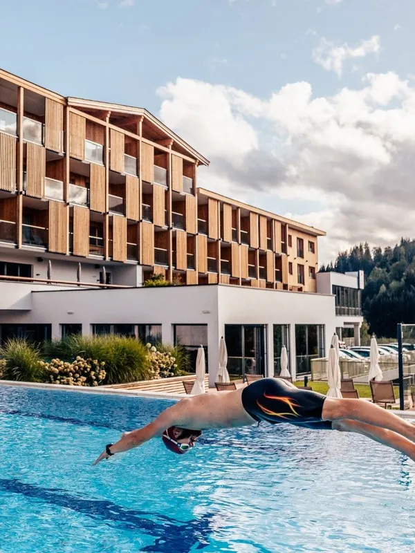 Mann springt in Außenpool vor Hotelgebäude mit Holzfassade
