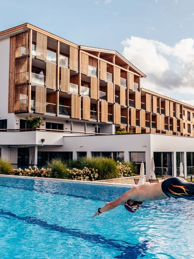 Mann springt in Außenpool vor Hotelgebäude mit Holzfassade
