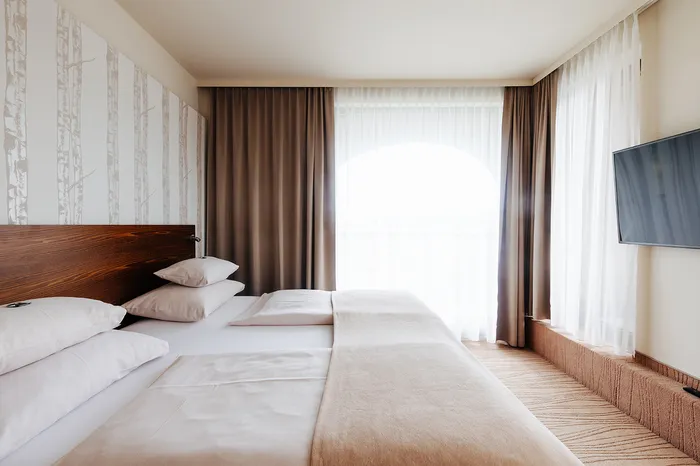 Hotelzimmer mit Doppelbett, Holzkopfteil, Vorhängen und Wandfernseher