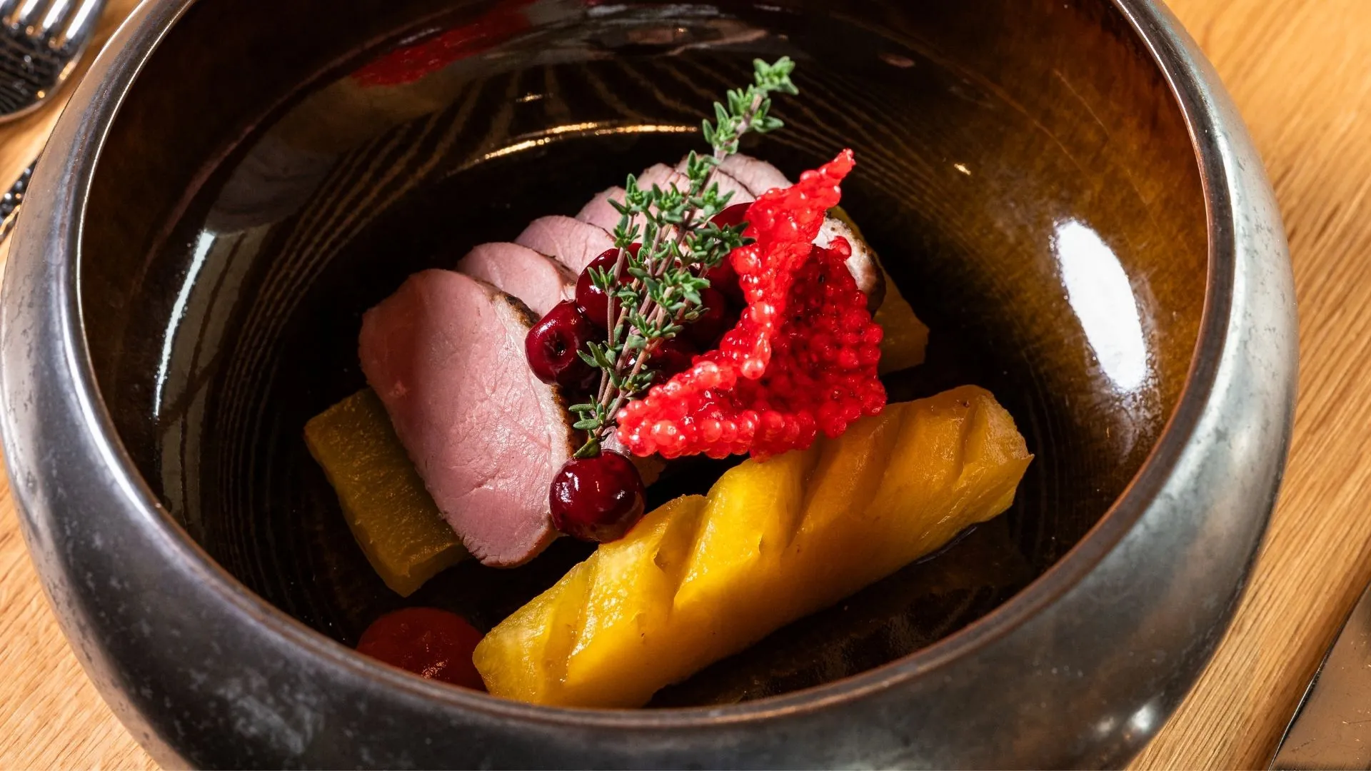 Angerichtetes Fleischgericht mit Kürbis, Beeren und Kräutern in dunkler Schale