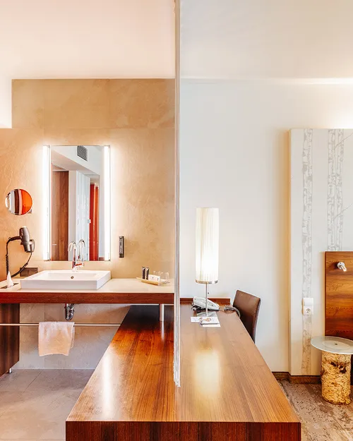 Hotelzimmer mit offenem Bad, orangefarbener Wand und Doppelbett mit Birkenmuster-Tapete
