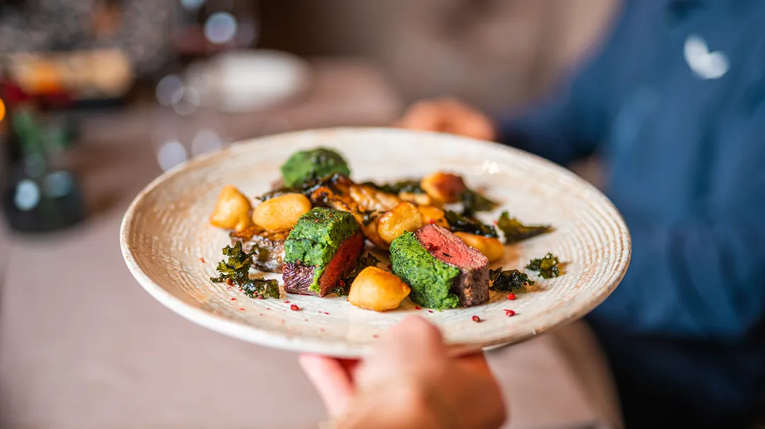 Serviertes Gericht mit rosa gebratenem Fleisch, Grünkohl und Gnocchi auf einem Teller