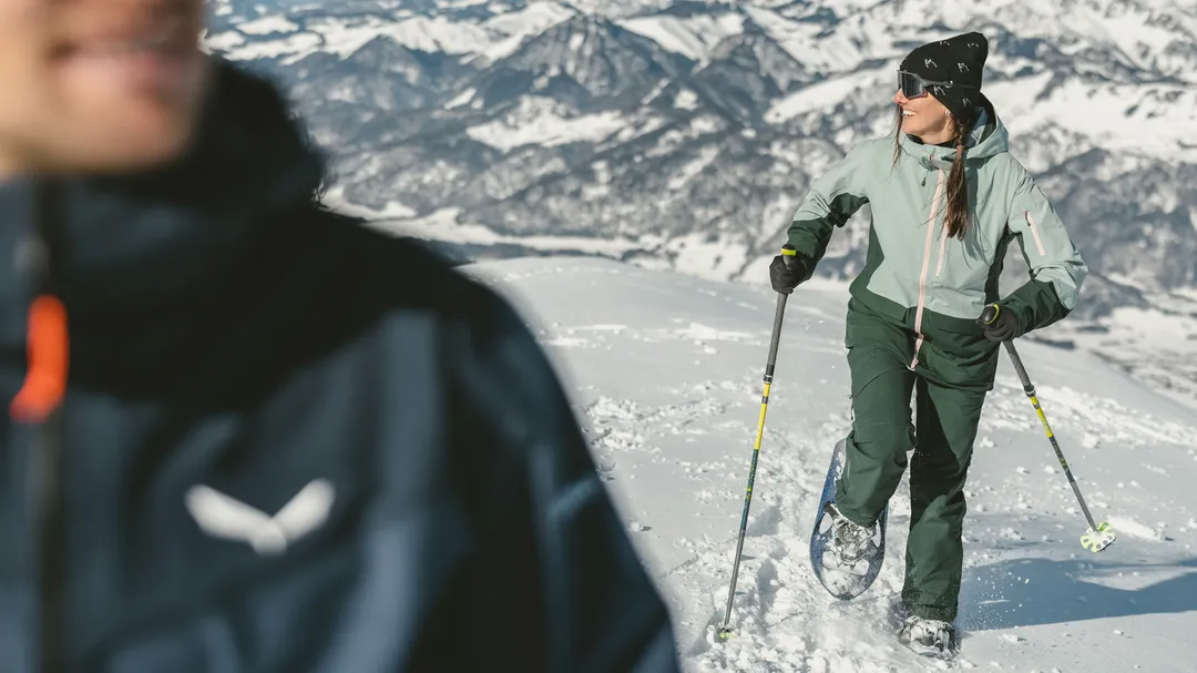 Schneeschuhwanderin mit Stöcken vor winterlichem Bergpanorama