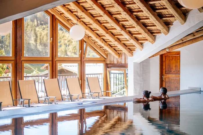 Pärchen entspannt im Hallenbad mit Holzdach und Panoramafenstern