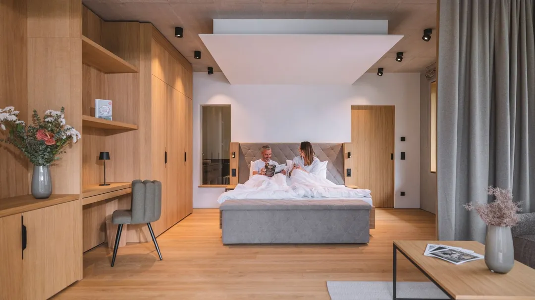 Paar sitzt im Bett in modernem Hotelzimmer mit Holzverkleidung