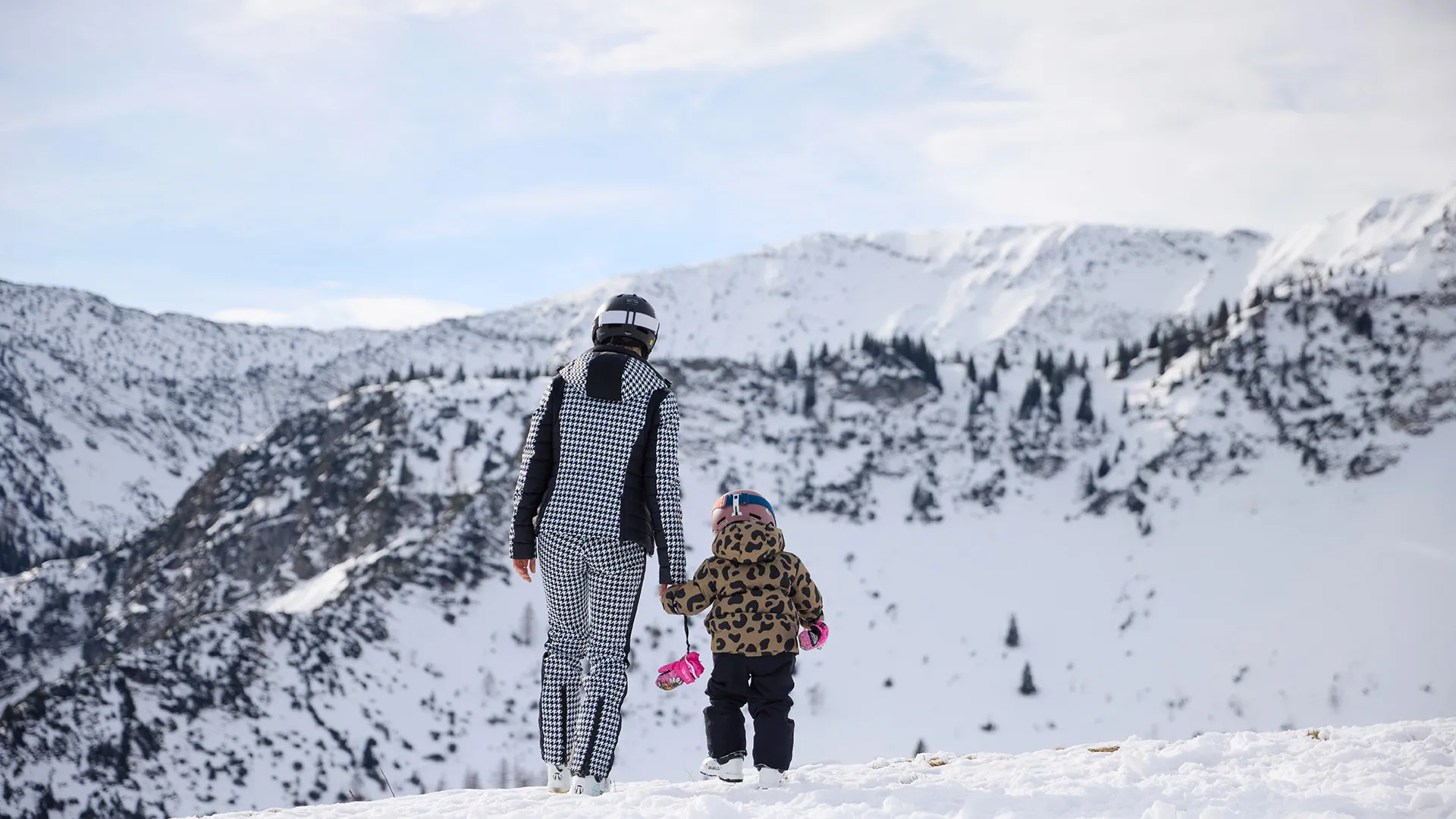 Mutter und Kind in Skibekleidung wandern durch verschneite Berglandschaft