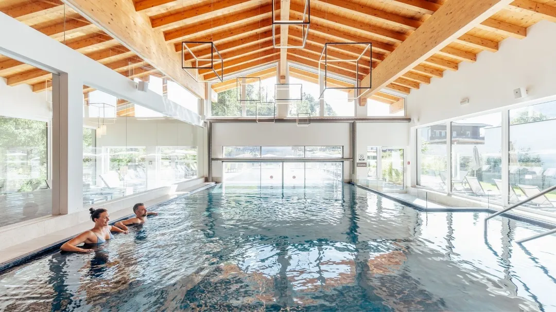 Pärchen im Hallenbad mit Holzdachkonstruktion und Panoramafenstern