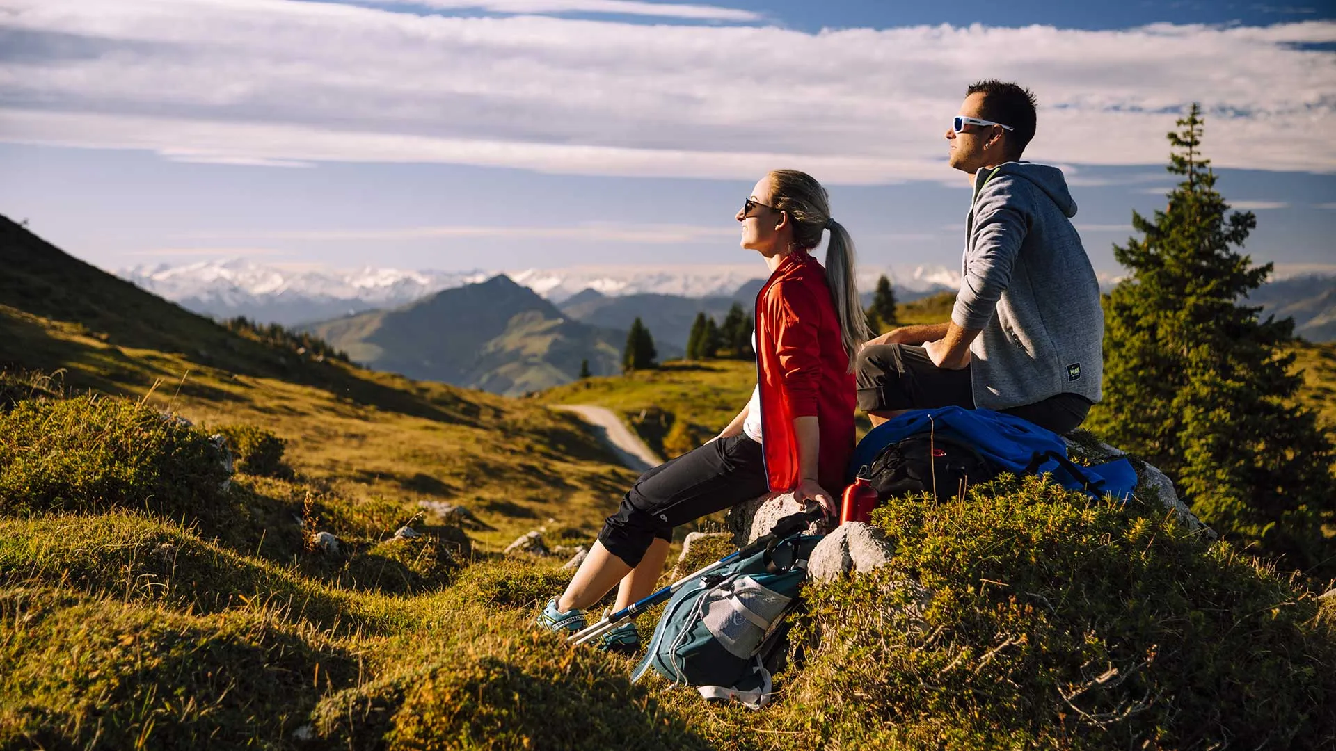 Wanderpaar sitzt rastend auf einem Felsen mit Blick auf Berge