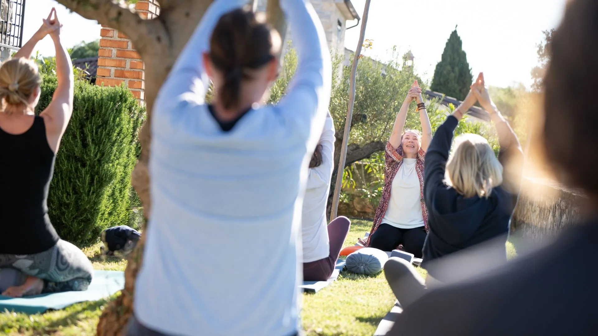 Gruppe bei Yoga-Übung im Freien mit erhobenen Armen im Garten