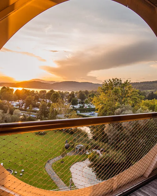 Sonnenuntergang über See und Garten, Blick durch rundes Balkonfenster