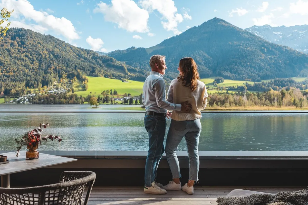 Paar blickt von der Terrasse auf einen See und Berge
