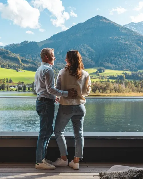 Paar blickt von der Terrasse auf einen See und Berge