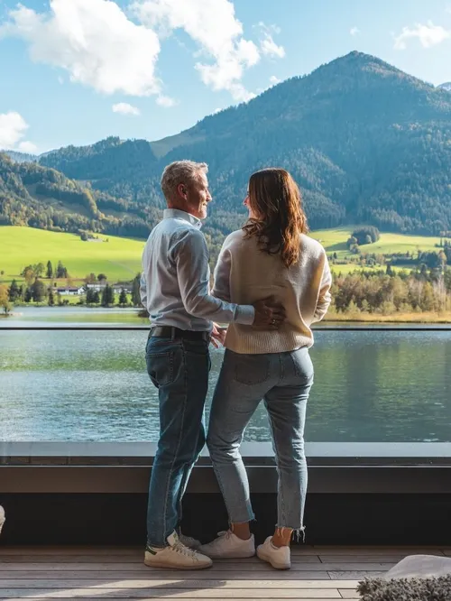 Paar blickt von der Terrasse auf einen See und Berge