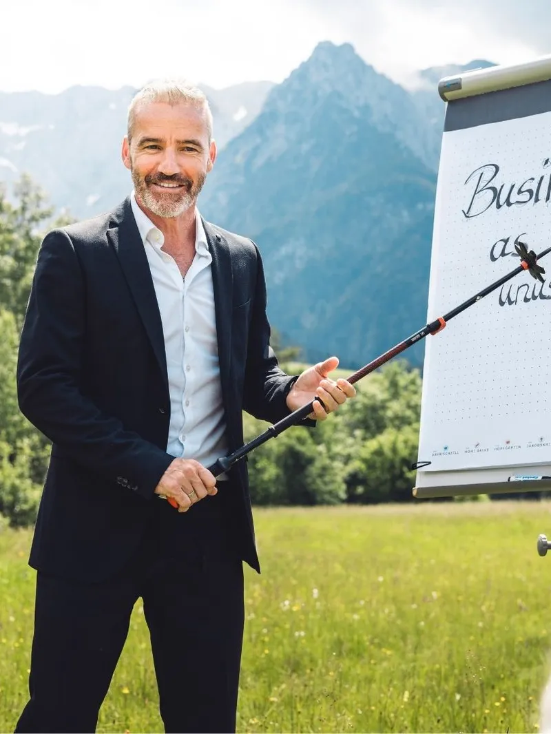 Mann im Anzug präsentiert vor Flipchart im Freien mit Bergpanorama