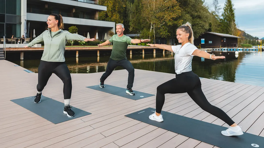Yogastunde auf einem Steg am See vor einem Hotel