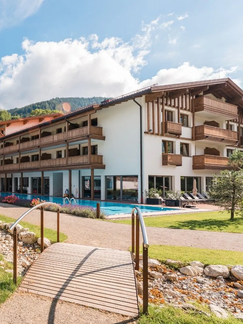 Hotelgebäude mit Außenpool und Liegewiese vor Bergkulisse