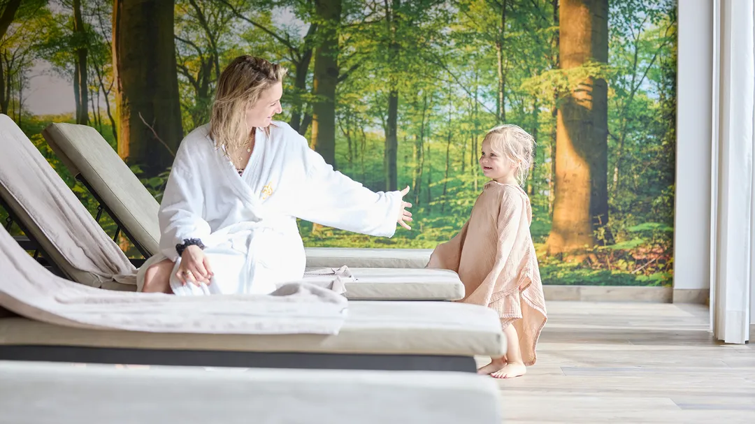 Mutter im Bademantel und Kind im Ruhebereich mit Waldmotiv-Wand