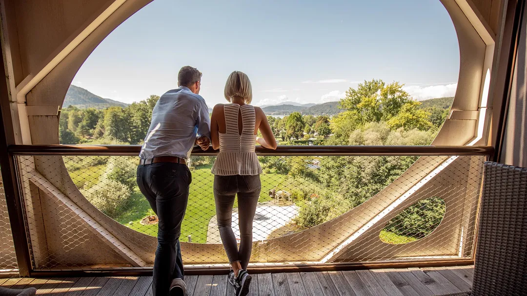 Paar blickt vom Balkonfenster auf Garten und Landschaft
