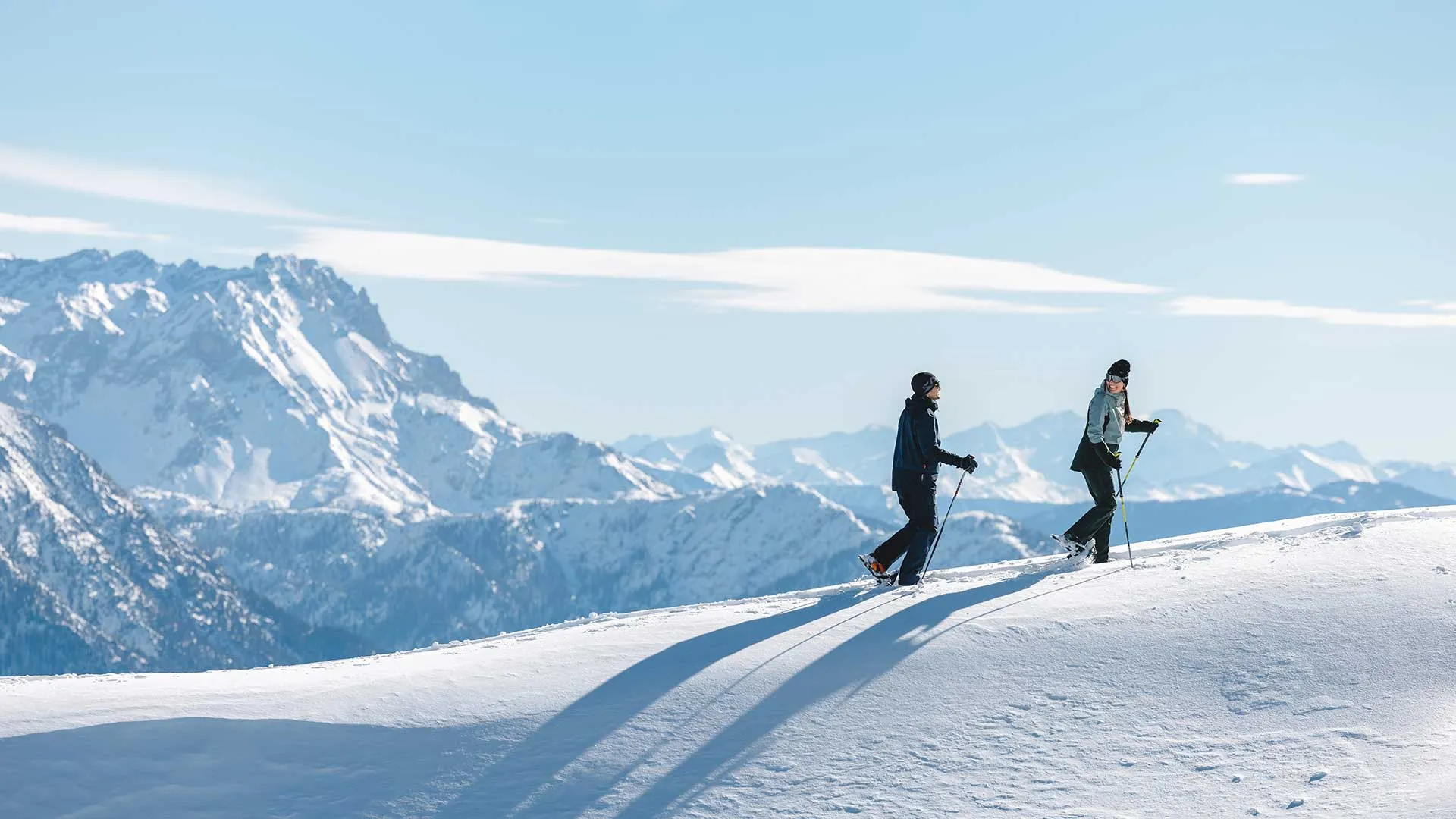 Zwei Personen beim Schneeschuhwandern auf einem Bergkamm vor Alpenpanorama