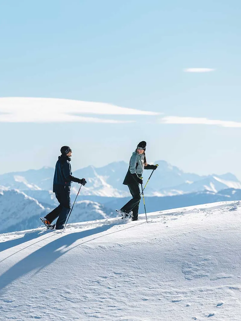 Zwei Personen beim Schneeschuhwandern auf einem Bergkamm vor Alpenpanorama