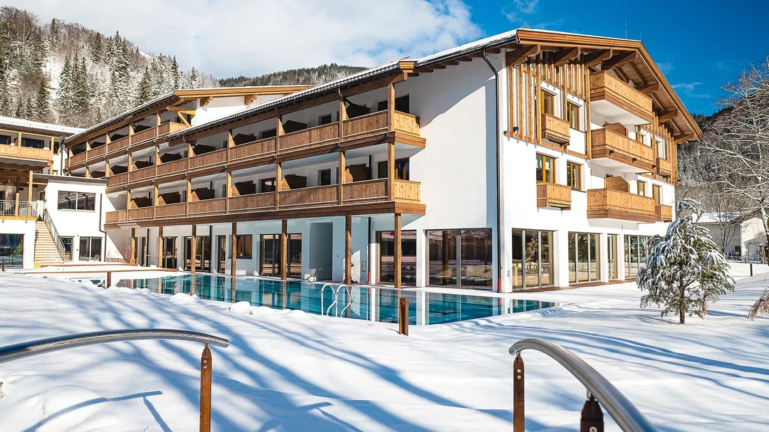Hotel mit Holzbalkonen und Außenpool im Schnee, umgeben von Bergen