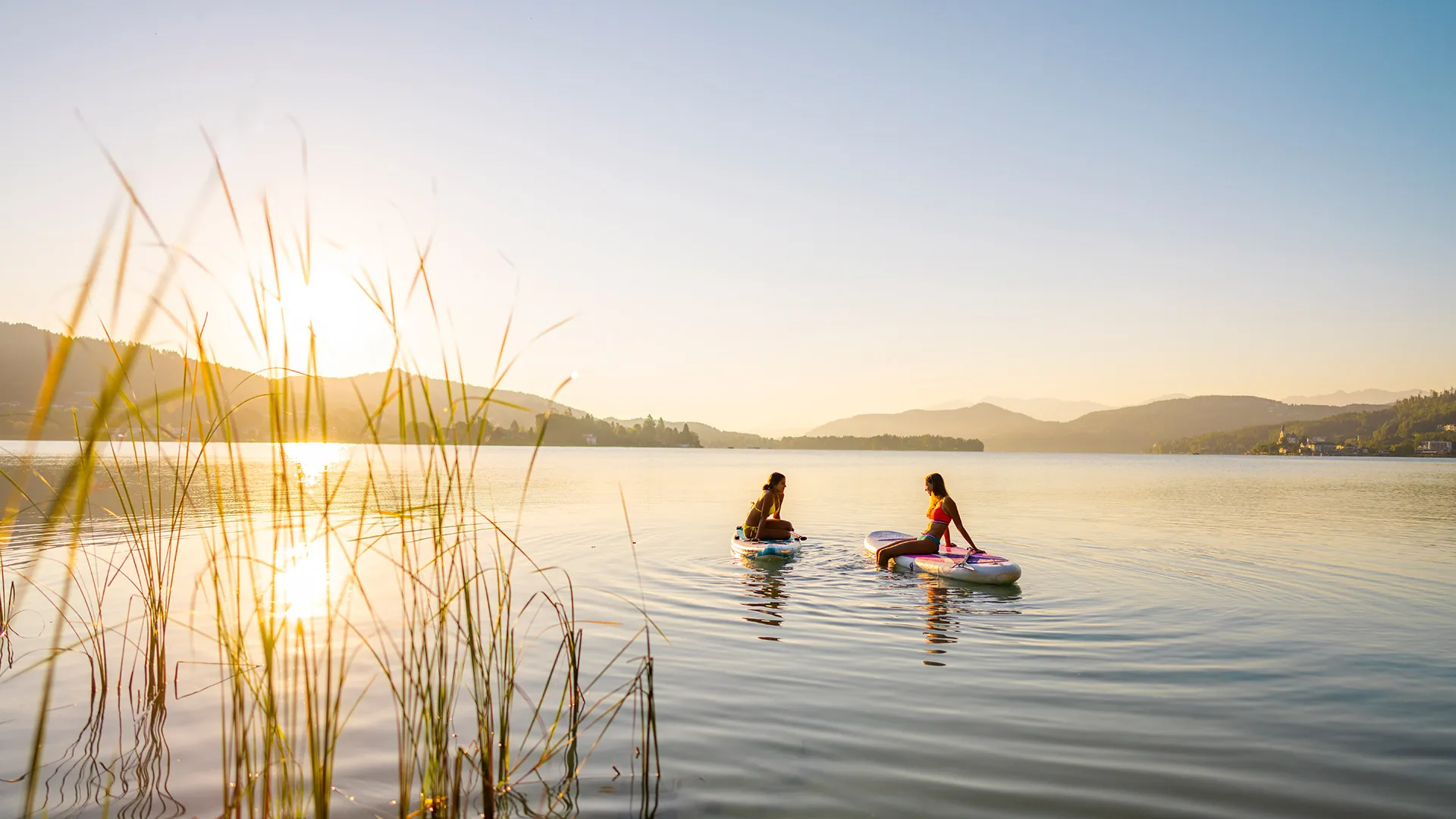 Zwei Frauen sitzen bei Sonnenuntergang auf SUP-Boards auf einem See
