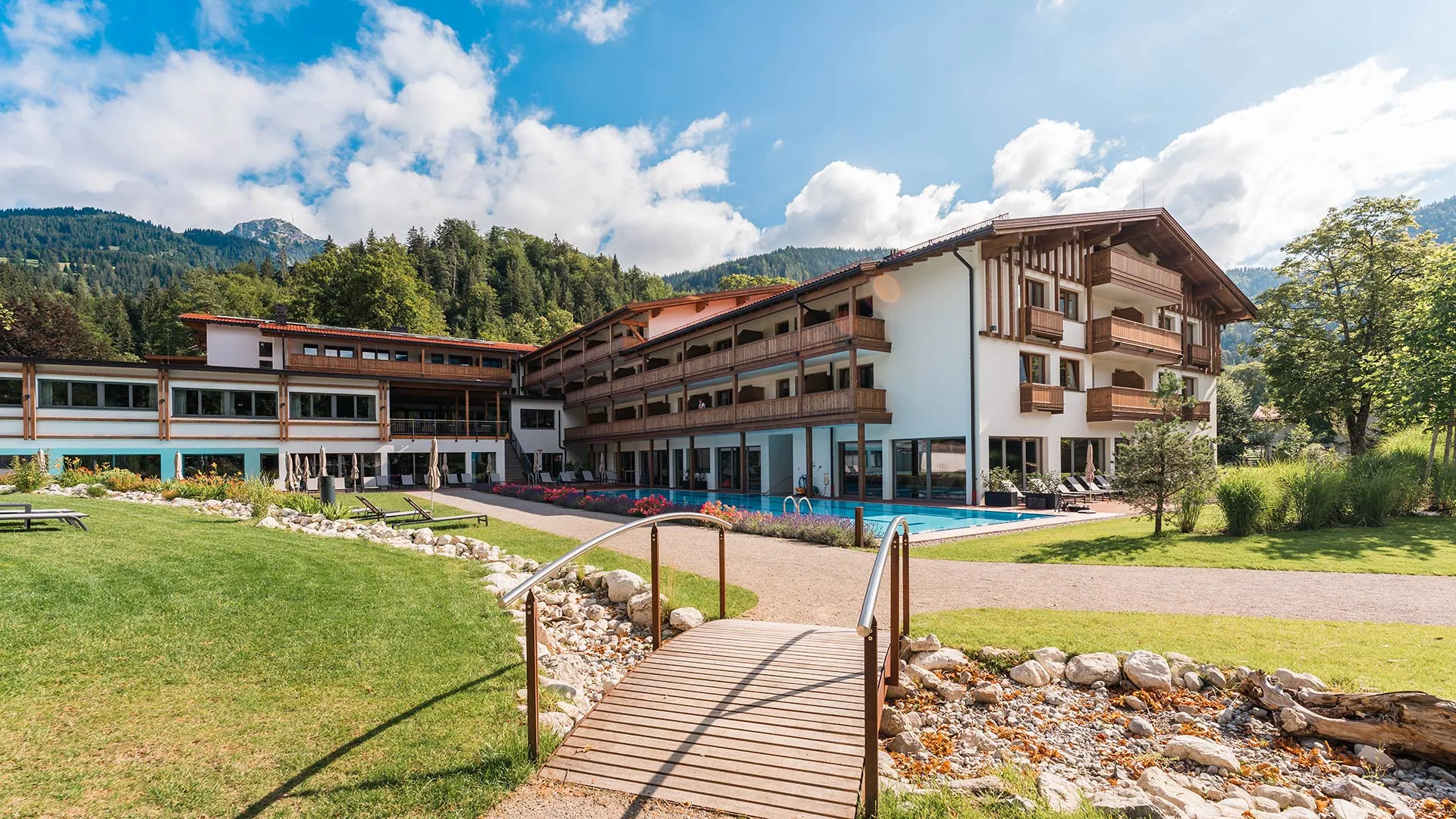 Hotel mit Außenpool und Garten im Sommer vor Bergkulisse
