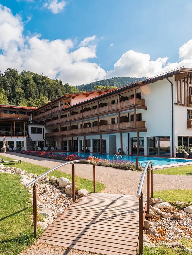 Hotel mit Außenpool und Garten im Sommer vor Bergkulisse