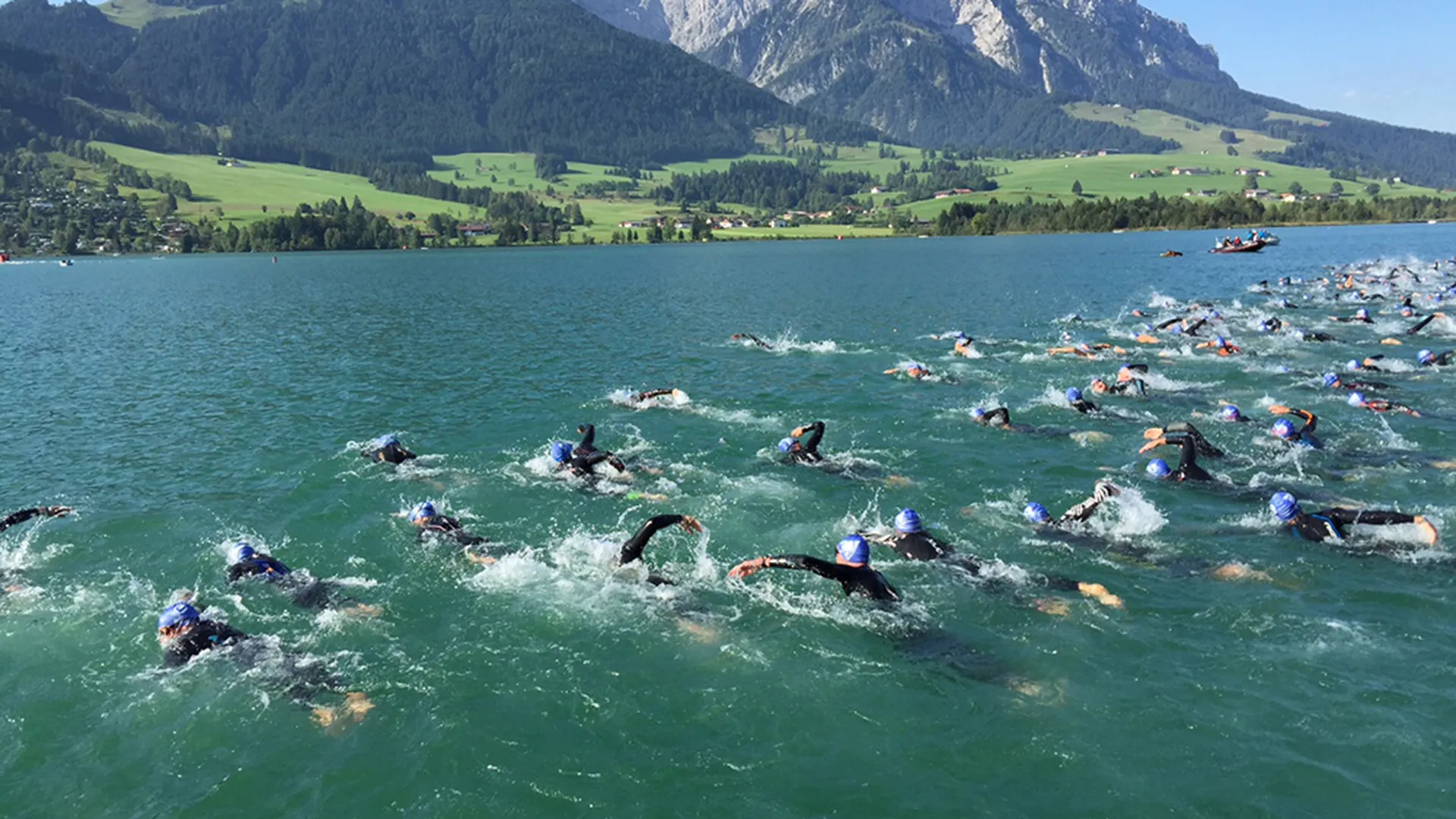 Schwimmer beim Triathlon-Start auf einem See vor Bergkulisse