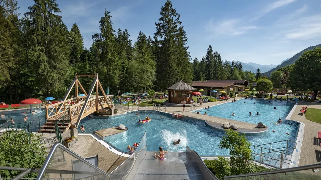 Freibad mit Rutsche, Pools und Bergblick, umgeben von Wald