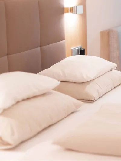Doppelbett mit Kissen im Hotelzimmer, im Hintergrund Sitzecke mit Tisch