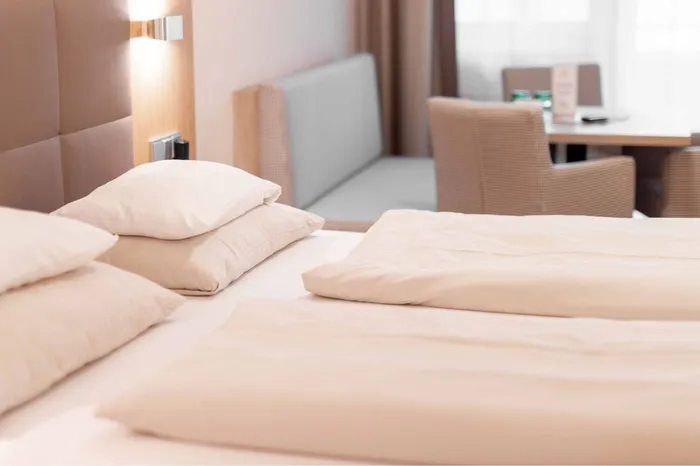 Doppelbett mit Kissen im Hotelzimmer, im Hintergrund Sitzecke mit Tisch