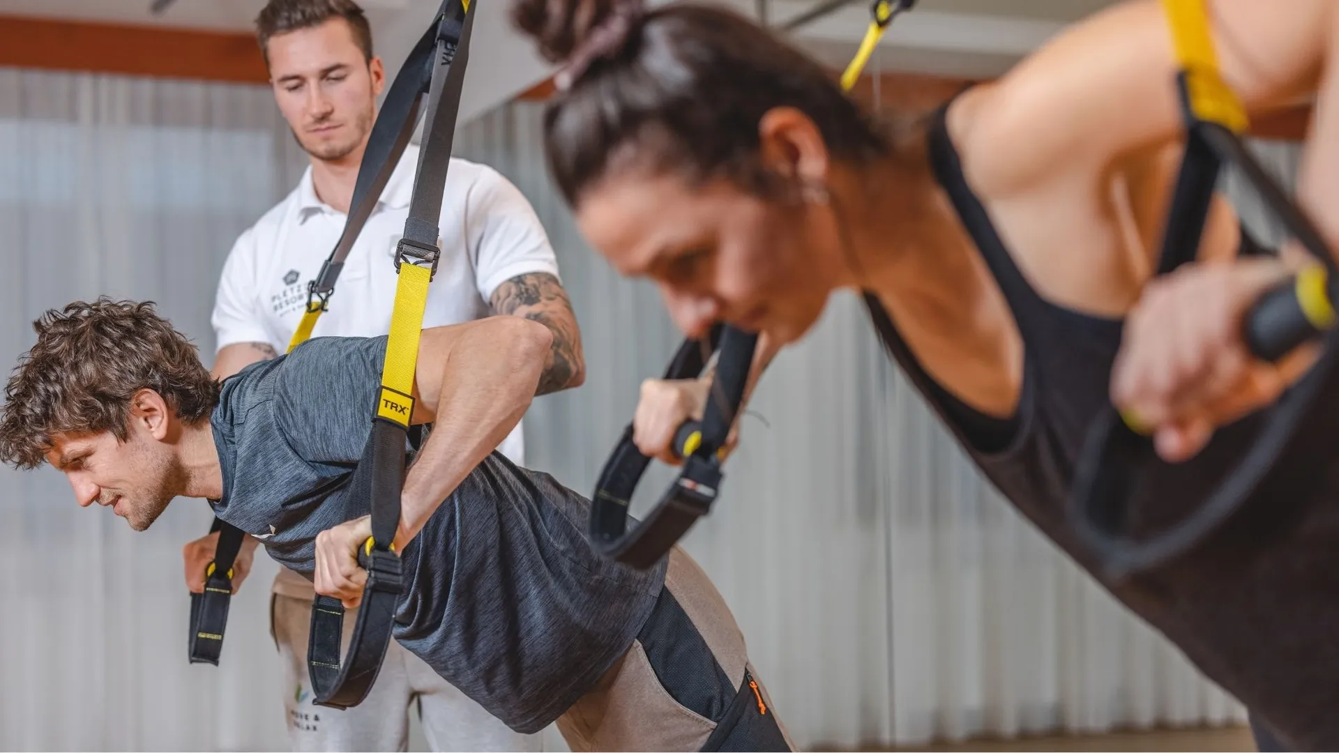 Personen trainieren mit TRX-Bändern unter Anleitung eines Trainers