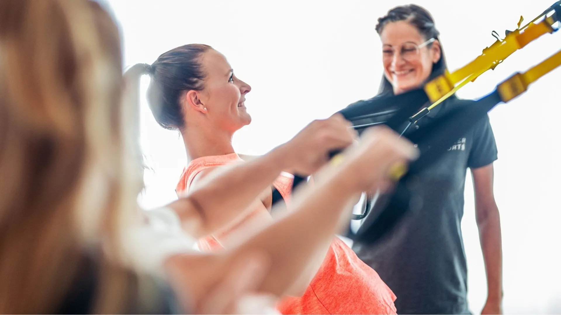 Frauen trainieren mit Trainerin an Schlingentrainer im Fitnessraum